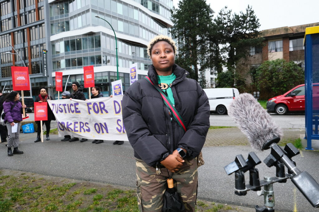 Boluwatife Shobiye, an SEIU member and a Skytrain cleaner, stands in front of a banner
